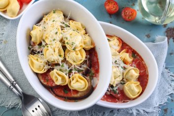 Pomidorowa zapiekanka z mięsnym tortellini, kozim serem, podawana na krążku pieczonego bakłażana